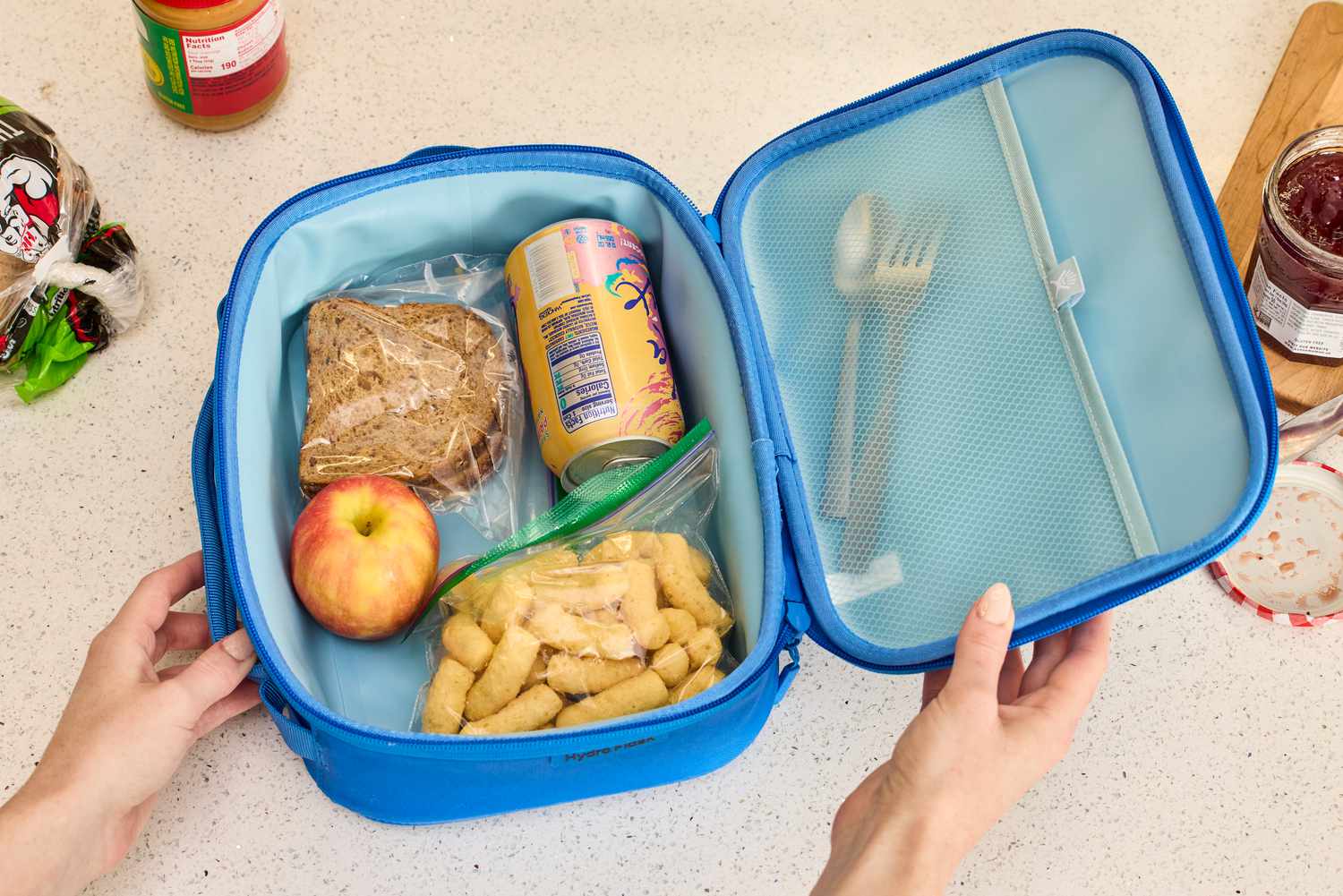 An open lunch box packed with snacks and silverware in a mesh compartment