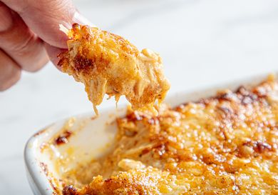 A closeup of a hand holding a scoop of baked dip with melted cheese from a dish