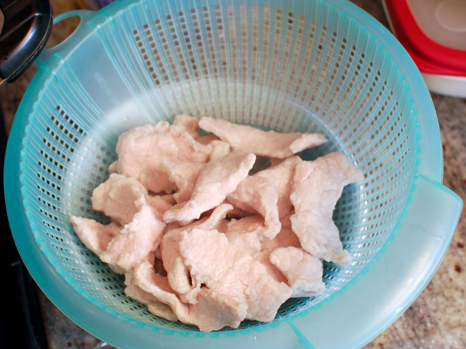 The velveted pork is transferred to a colander to drain.