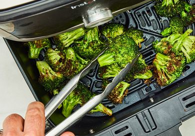 Broccoli being cooked in an air fryer with tongs
