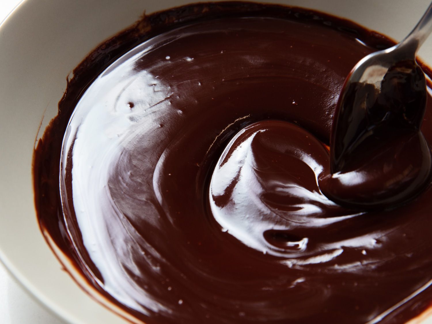 A chocolate glaze in a bowl being stirred by a spoon.