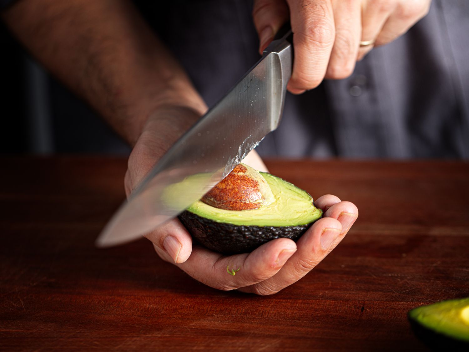 A person removing the pit from half of an avocado with a knife closeup on hands and the avocado