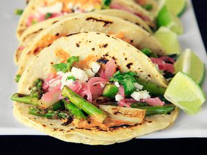 Closeup of Charred Asparagus Tacos With Creamy Adobo and Pickled Red Onions, served with lime wedges.