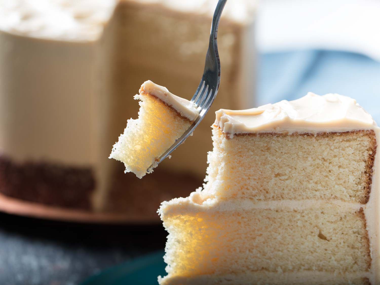A fork has lopped off a large bite from the topmost point of a slice of white cake.
