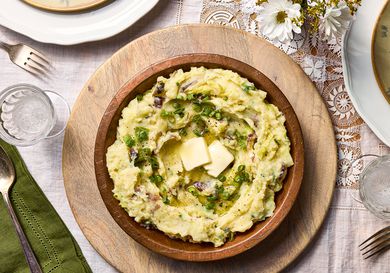 wooden bowl filled with colcannon with butter in it, on a lace tablecloth with flowers to the side
