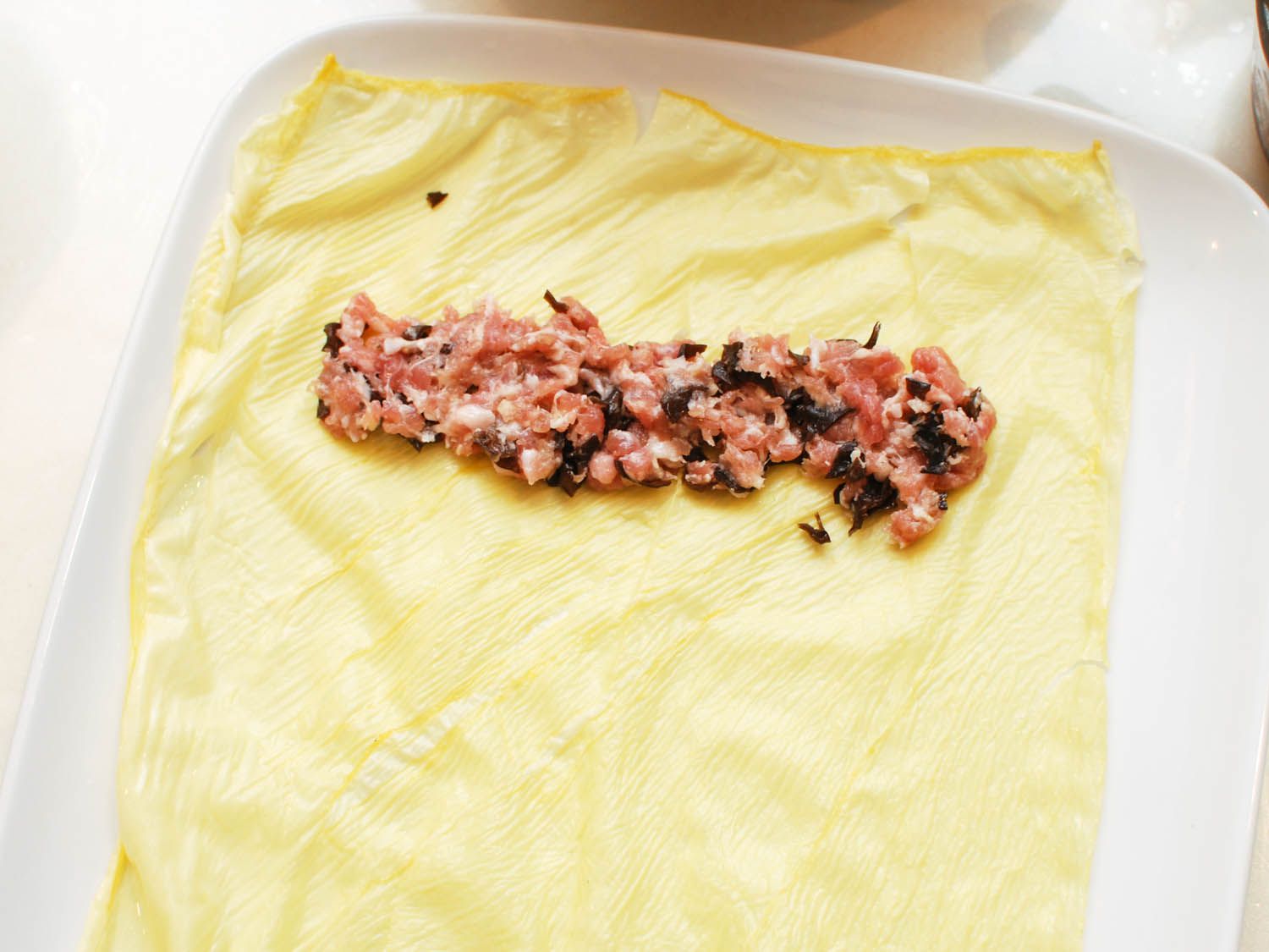 A long mound of pork filling is placed near the top of the bean curd sheet with a healthy margin on the top and sides for sealing the filling in.