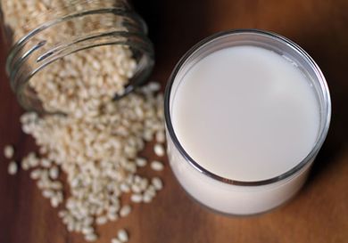 A glass of DIY rice milk. A glass canning jar of dry rice grains has been artfully spilled on the countertop nearby.