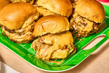 Bright green platter of sliders with overflowing cheese and onions 