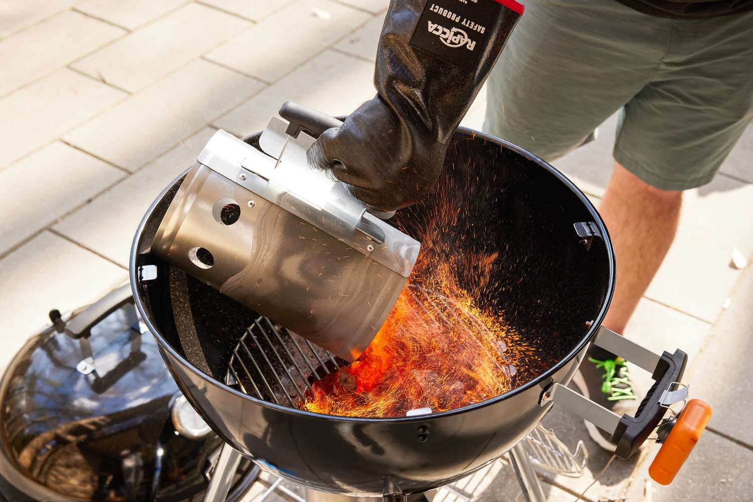 Flaming coals are poured onto the charcoal grate of a grill