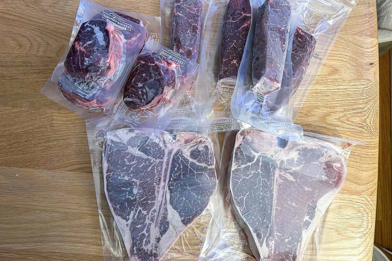 Various cuts of vacuumsealed Omaha Steaks raw meat on a wooden surface including steak cuts and filet portions