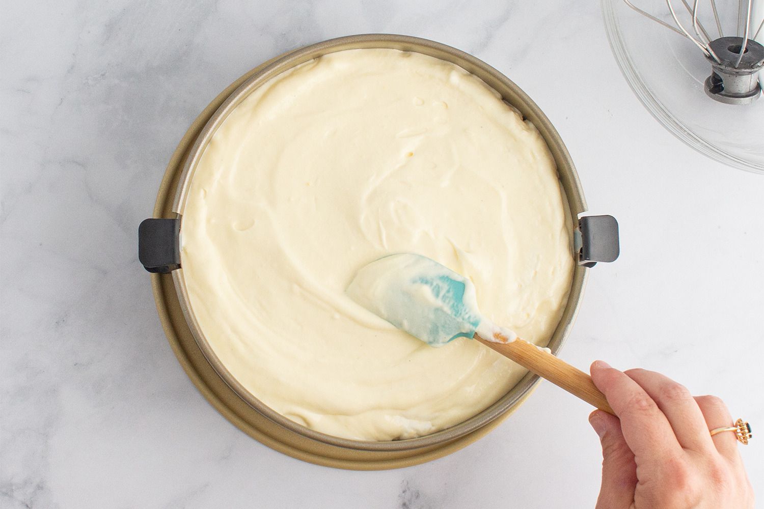 A person spreading cheesecake batter in a springform pan.
