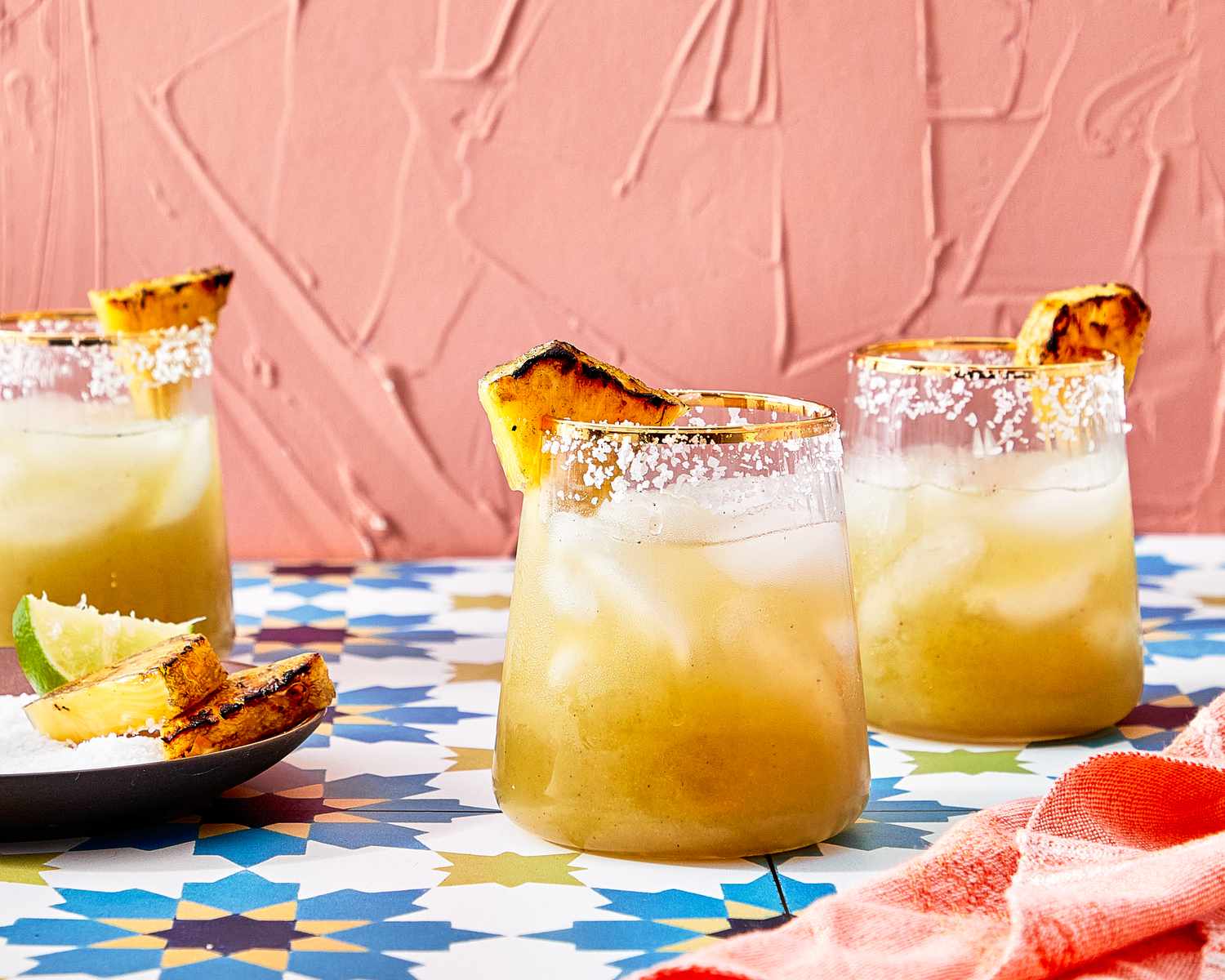 Three glasses of margarita with grilled pineapple garnishes on a colorful table
