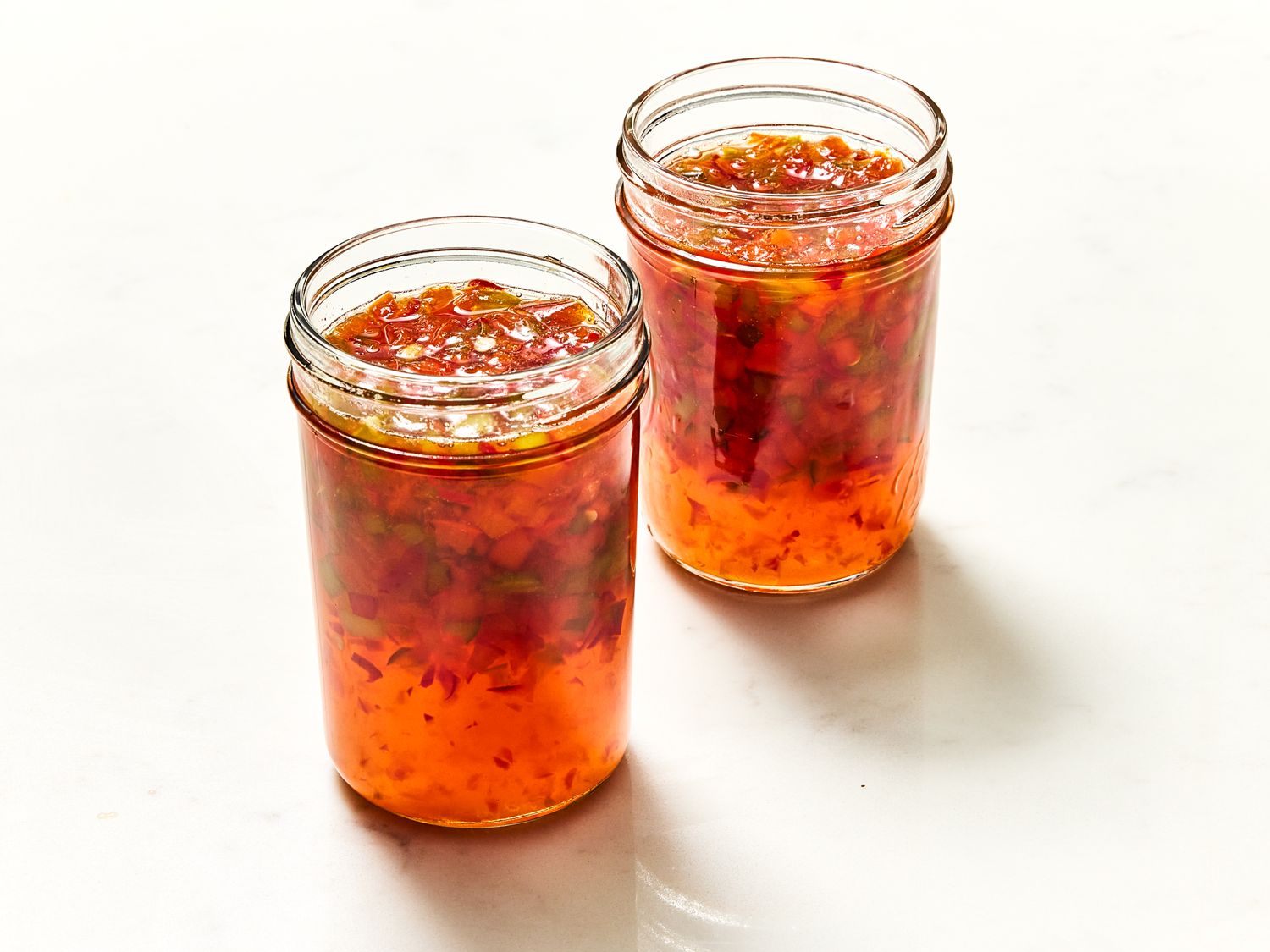 Two jars of homemade pepper jelly placed on a white surface