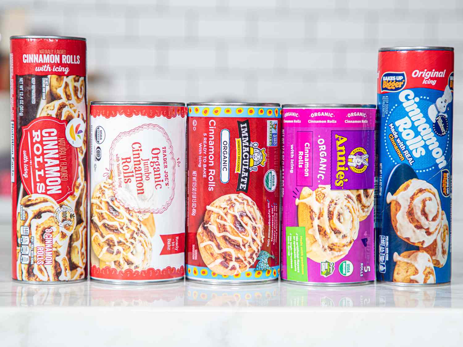 An assortment of canned cinnamon roll products from different brands lined up on a countertop