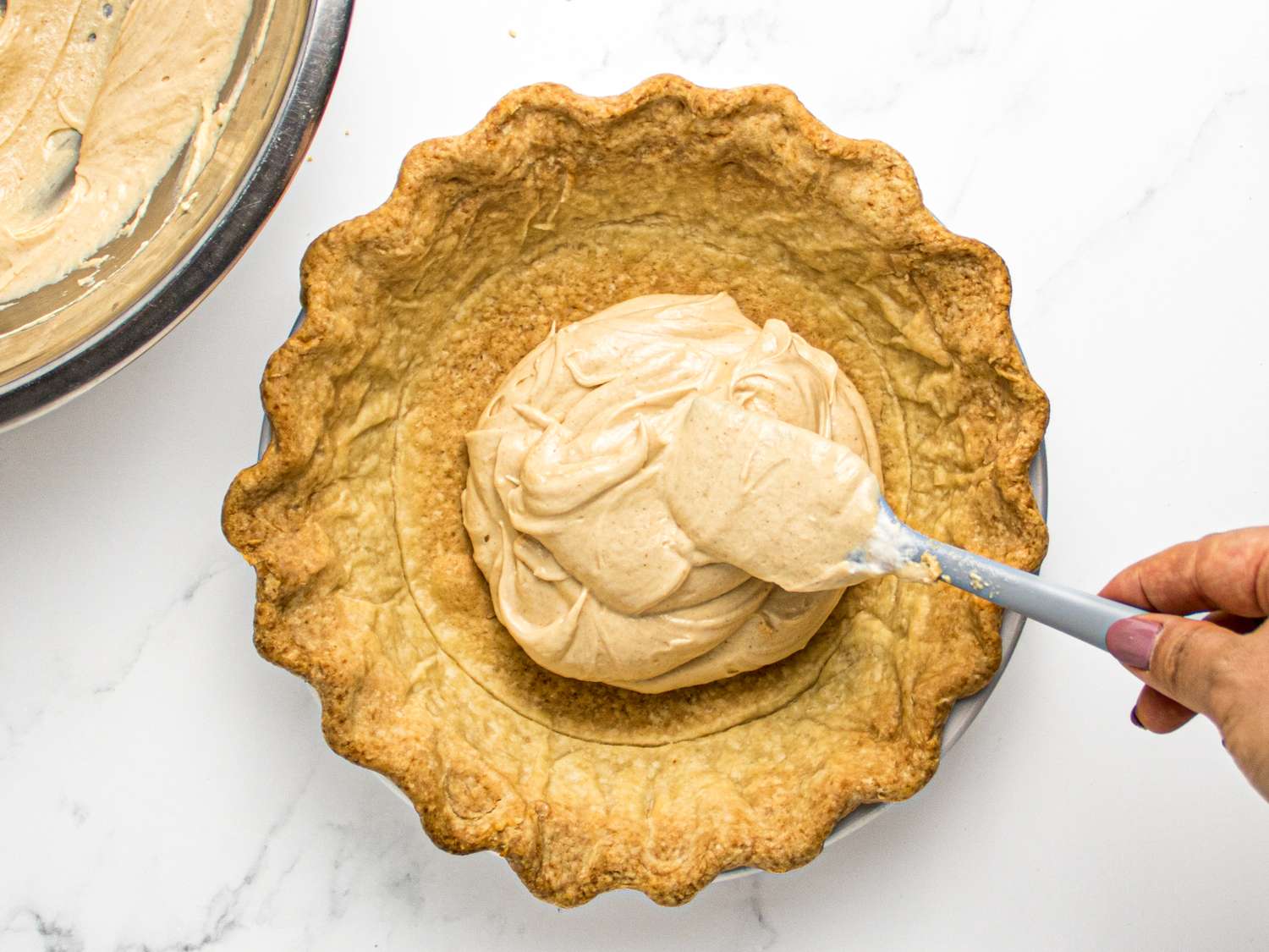 A hand spreading filling in a pie crust with a spatula