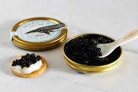 a tin of Marky's royal white sturgeon caviar next to a blini topped with crème fraîche and a scoop of caviar