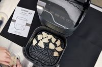 A person inserts frozen food inside of a Cosori air fryer.