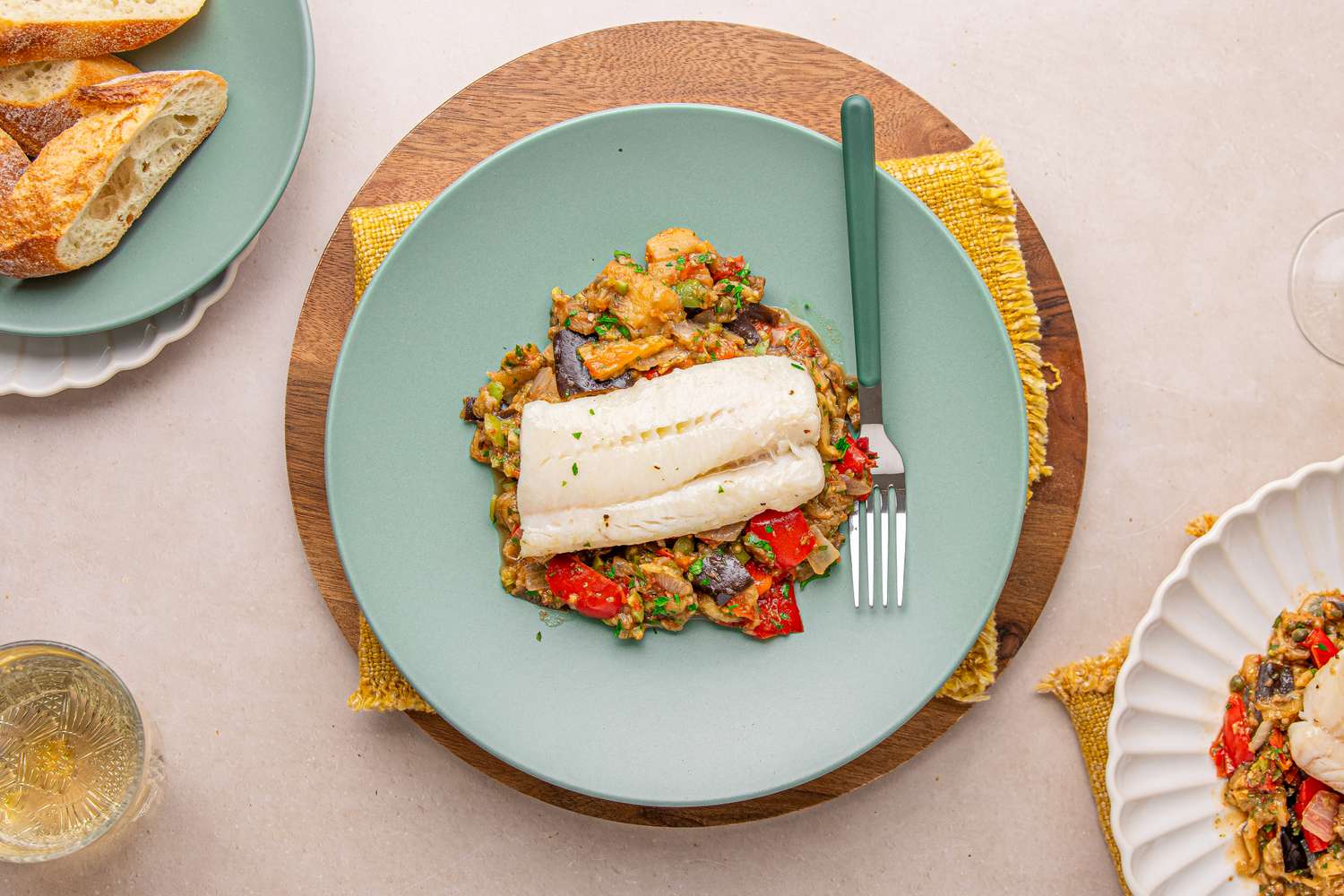 A serving of cod on caponata with bread and wine in the setting