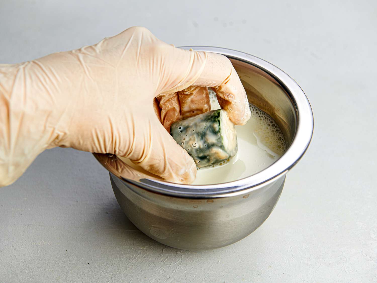 A gloved hand holding a stuffed jalapeÃ±o ring which has been dipped in milk, then flour, and then back in milk.