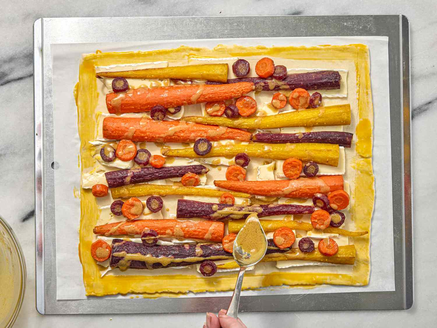 Hand holding a spoon drizzling sauce on savory carrot tart