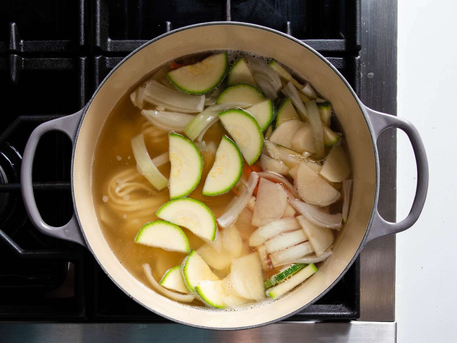 Adding squash, potatoes, and noodles to broth in Dutch oven.
