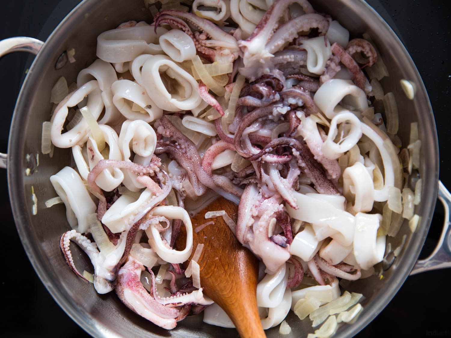 Overhead view of squid, onions, and garlic cooking in a large saucepan.