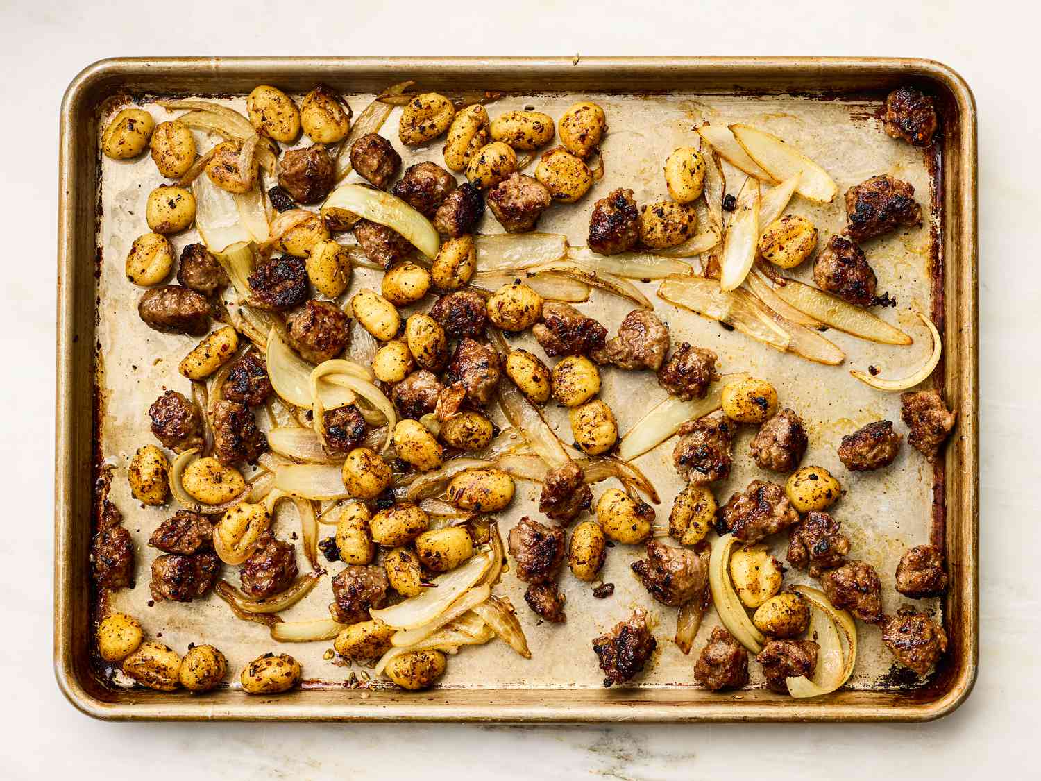 Sheet pan with cooked gnocchi, onion slices, and browned sausage pieces