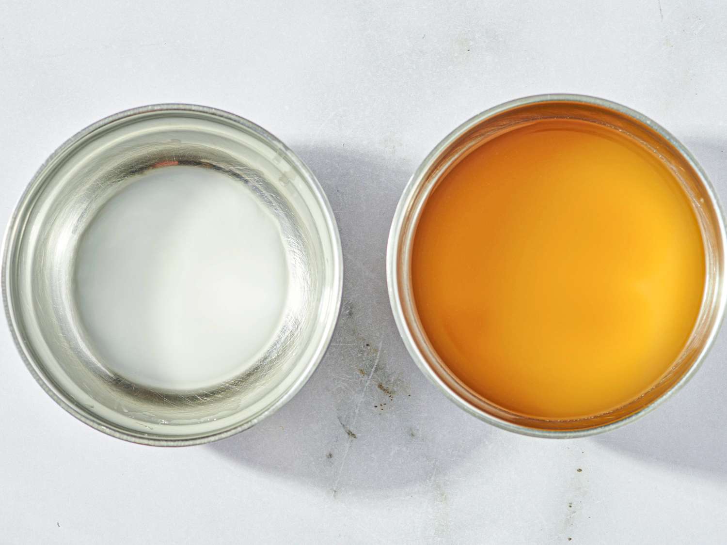 Two bowls one with a lightcolored liquid and one with a darker orange liquid placed side by side on a surface