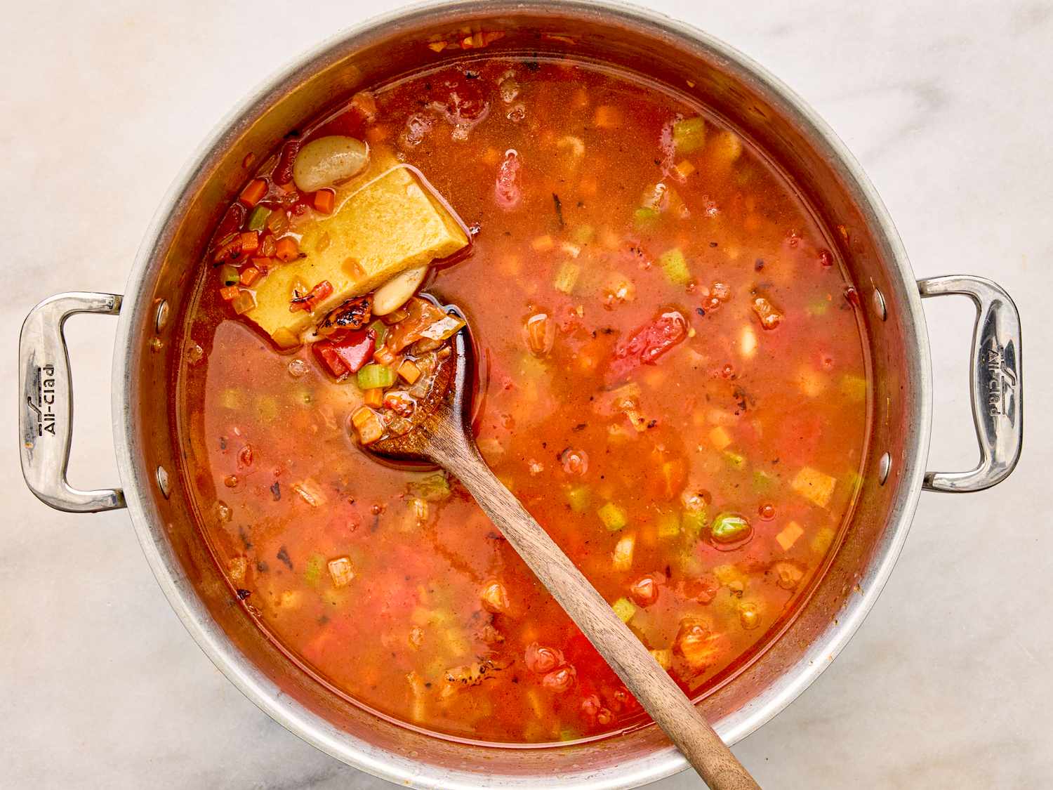 A pot containing vegetable and bean soup with a wooden spoon