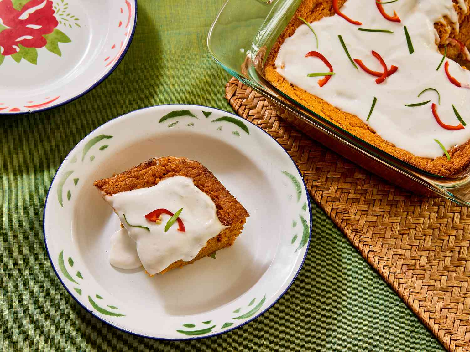 square of squash souffle in a white dish, and glass baking pan of whole souffle on a green fabric surface and rattan heat pad