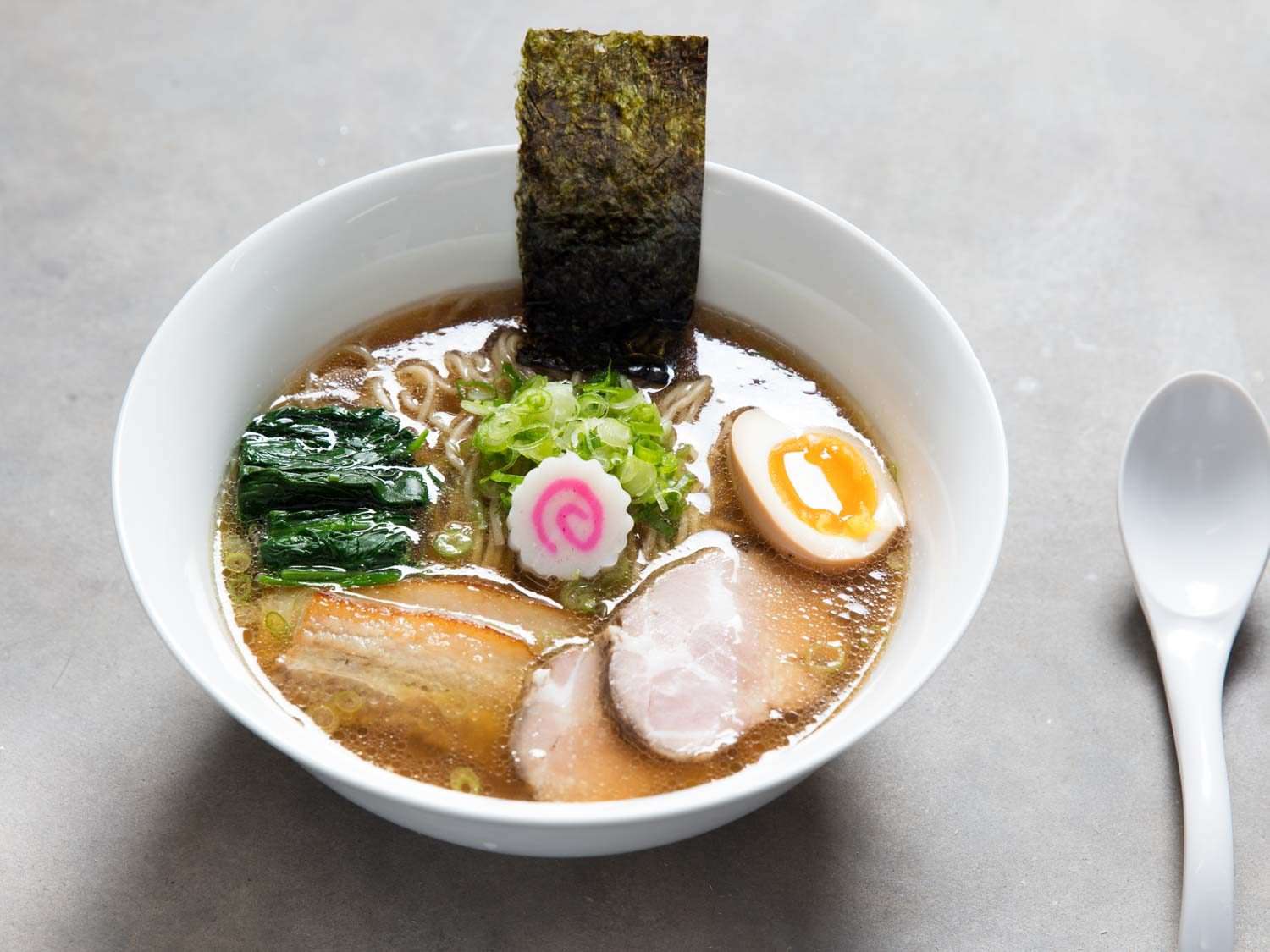 Bowl of shoyu ramen garnished with seaweed, sliced scallion, fish cake, soft-boiled egg, and pork