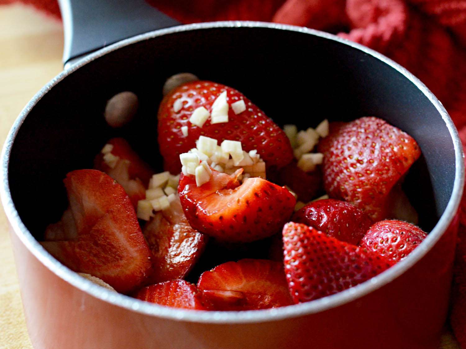 Pot filled with halved fresh strawberries and chopped garlic.