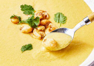 A spoonful of creamy corn soup with garnishes including herbs and toasted corn