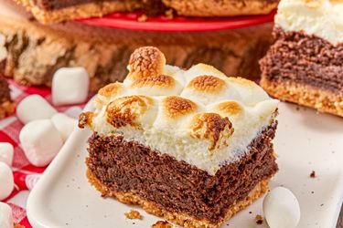 A slice of brownie topped with toasted marshmallows on a plate surrounded by mini marshmallows