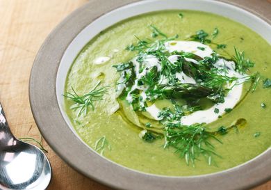 A bowl of cream asparagus and tarragon soup chopped tarragon,fennel frond, asparagus tips, a drizzle of olive oil, and a touch of crème fraîche.