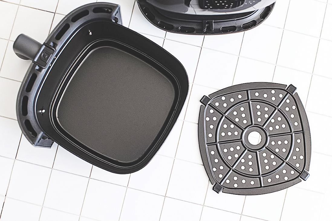 An open air fryer basket with its detachable tray displayed on a tiled surface