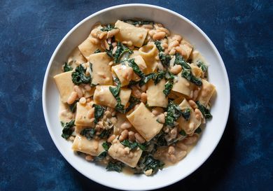 A bowl of paccheri pasta with flavorful sauce of beans and greens.