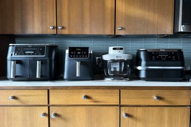 Four kitchen air fryers displayed on a countertop arranged in a row showcasing various models and designs