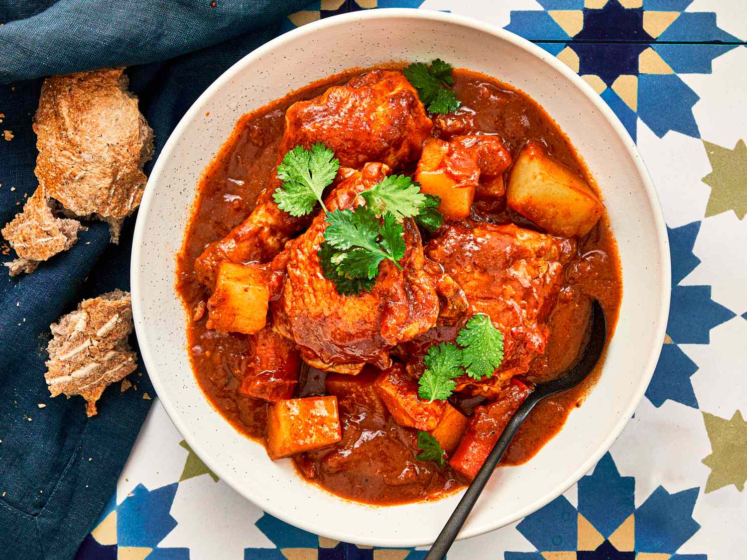A dish of Pollo Guisado served with potatoes and carrots garnished with parsley