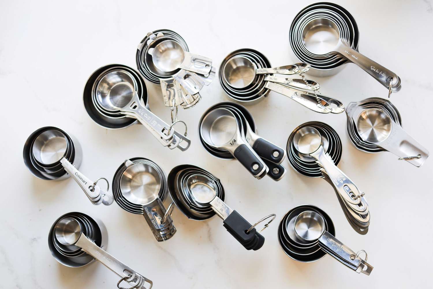 A number of stainless steel measuring cup sets on a marble kitchen countertop.