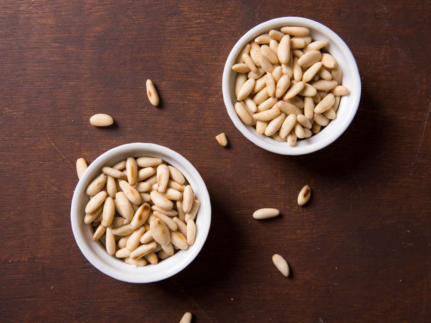 Two ramekins filled with pine nuts; the bottom ramekin contains toasted pine nuts.