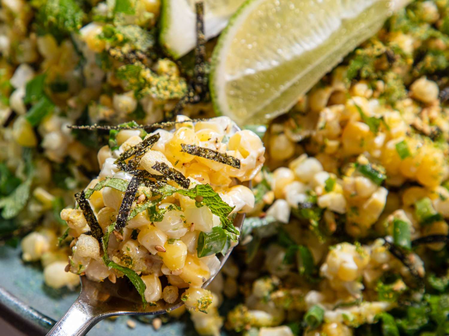 A dish of corn salad with herbs lime wedge garnish and nori strips visible
