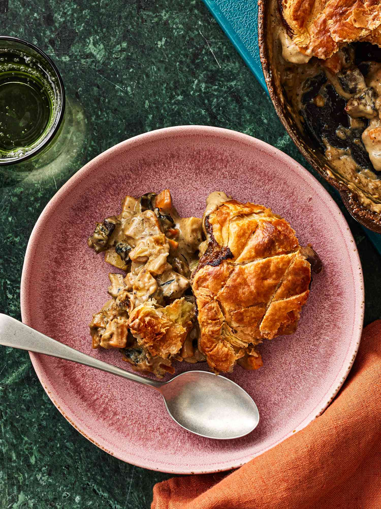 Serving of Mushroom Pot Pie on a muted pink plate,with full pot pie in a skillet on the side, and a rust colored napkin