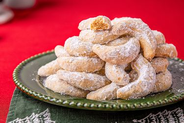 A stack of crescentshaped cookies dusted with powdered sugar arranged on a green plate placed over a festive napkin