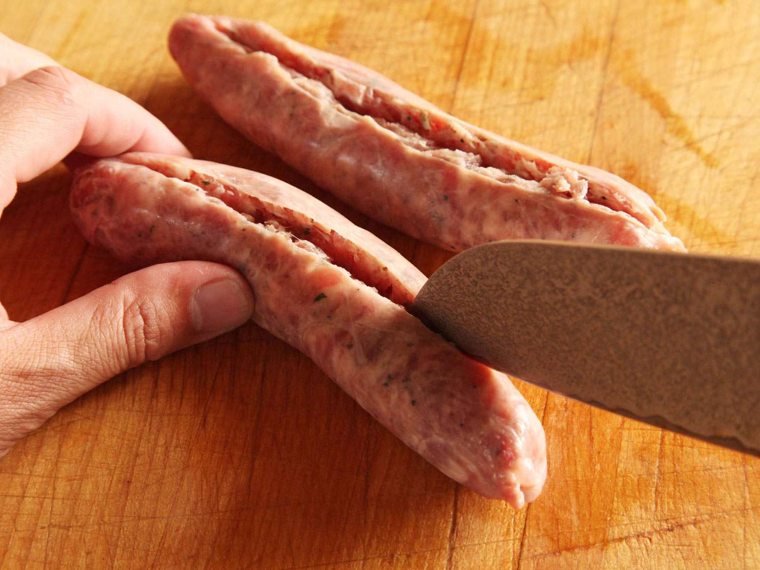 Using a chef's knife to slit sausage down the middle.