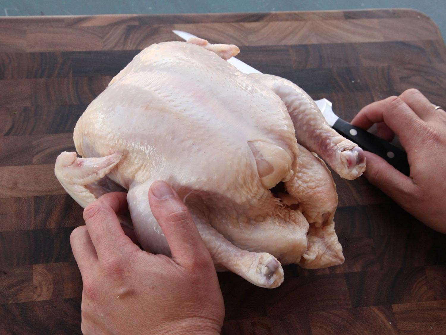 A whole chicken resting on a cutting board, with a pair of hands flanking it.