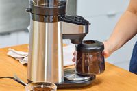 A person removes a canister of ground coffee from the OXO Brew Conical Burr Coffee Grinder With Integrated Scale