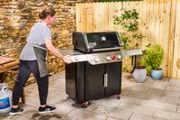 A person moves the Weber Genesis E-335 Gas Grill across the patio