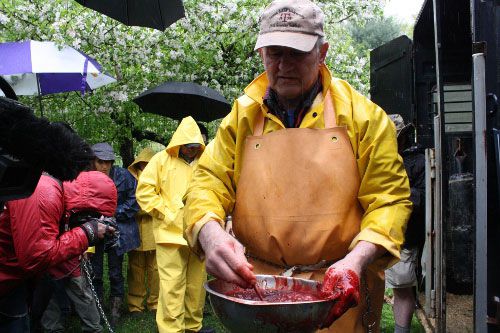 Hans the butcher in an apron stirring a bowl of pig's blood.