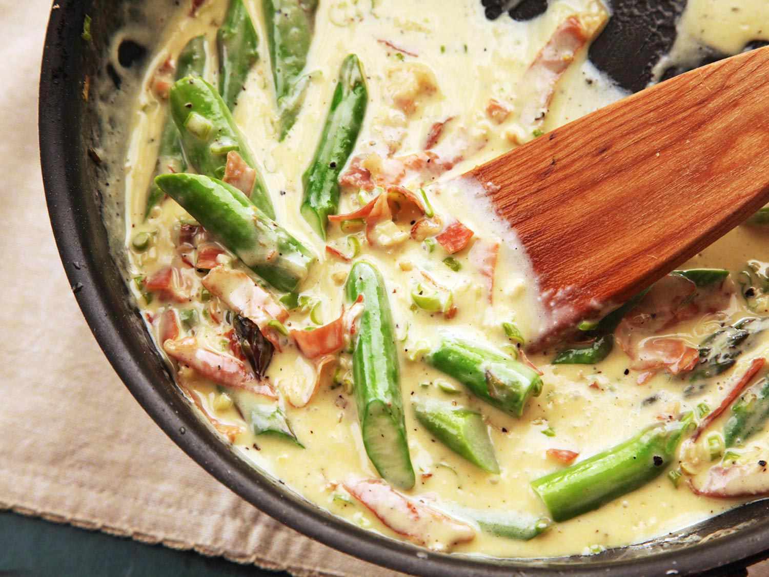 Stirring prosciutto, asparagus, and cream together in a pan to serve with gnocchi.